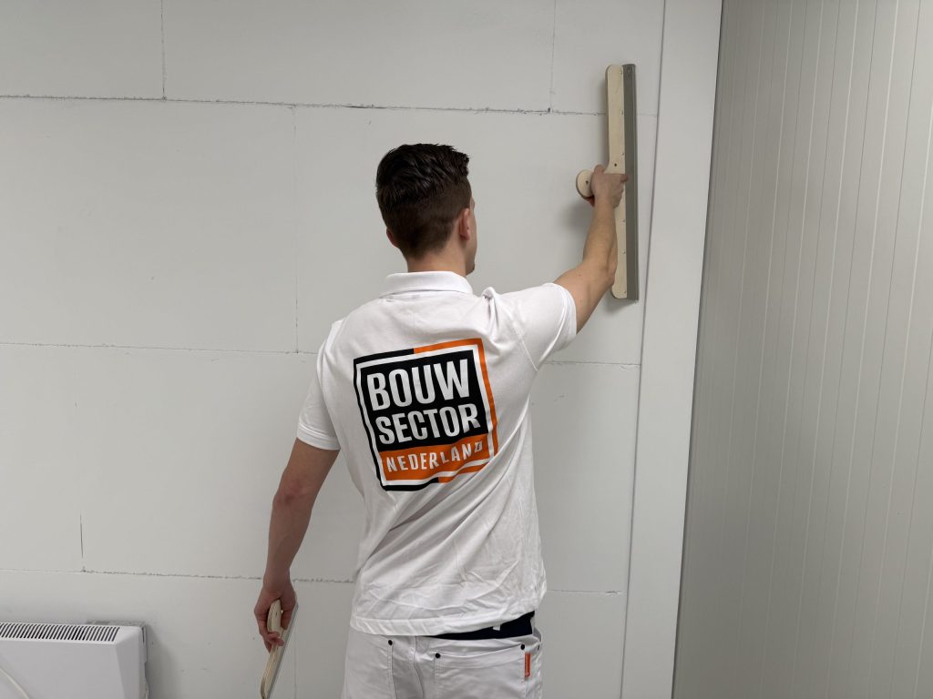 Stukadoor trekt met een lange spaan de bovenkant van een wand van gipsblokken vlak